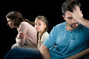 Parents fighting and angry with young female child sitting between them. Signifies the challenges of divorce with children.