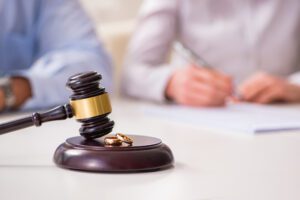 Wedding rings sitting on judicial gavel with man and woman in the background. Signifies divorce or annulment.