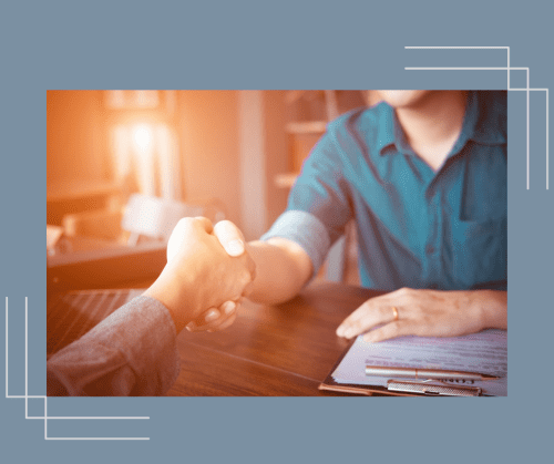 Divorce coach shaking hands with a client over a desk. Sunlight in the background. 