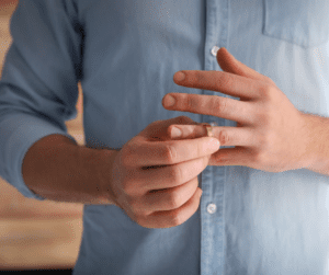White man in blue button up shirt taking off gold wedding band.