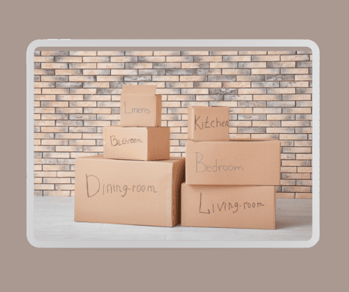 Moving boxes with room labels stacked against a brick wall.