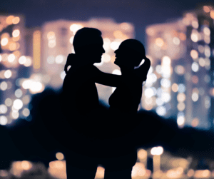 Shilouette of couple embracing in front of cityscape.