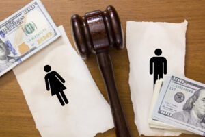 Image of man and woman with judicial gavel between and stacks of money on both sides. Signifies asset division in divorce.