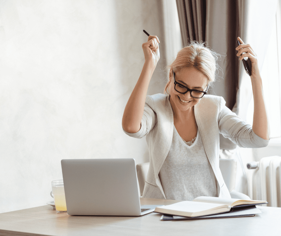 Young white woman celebrates at a table in front of a laptop