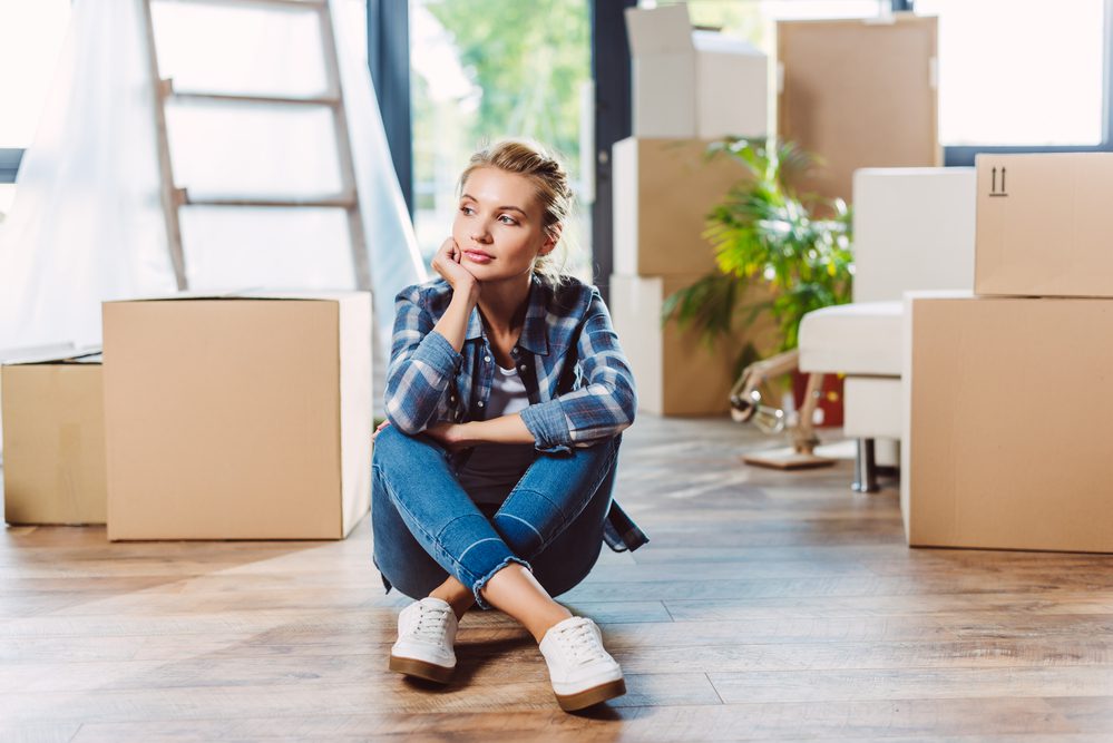 Young pretty woman sitting on the floor surrounded by moving boxes.