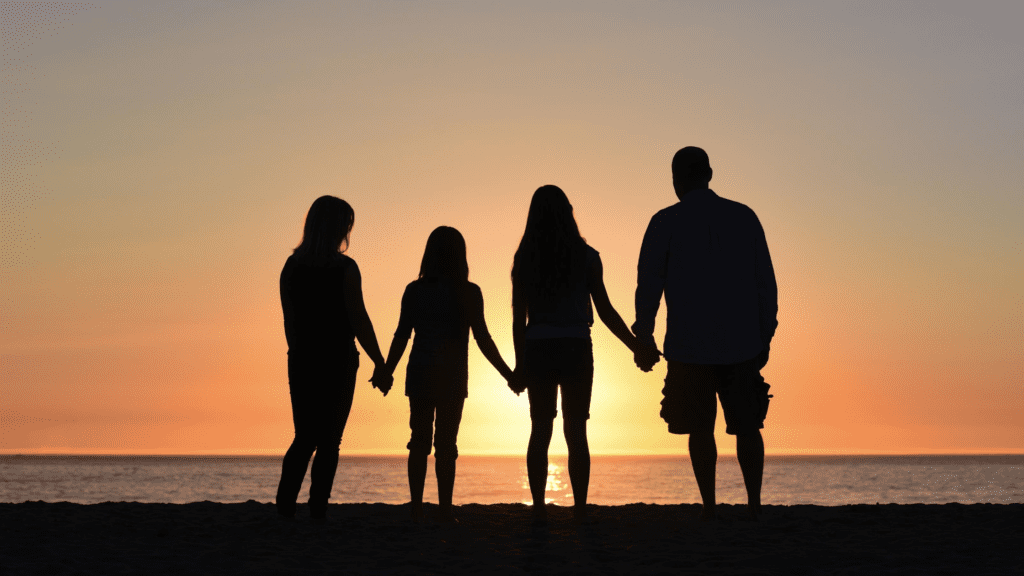 mother, two daughter, and dad holding hands and silhouetted before a sunset