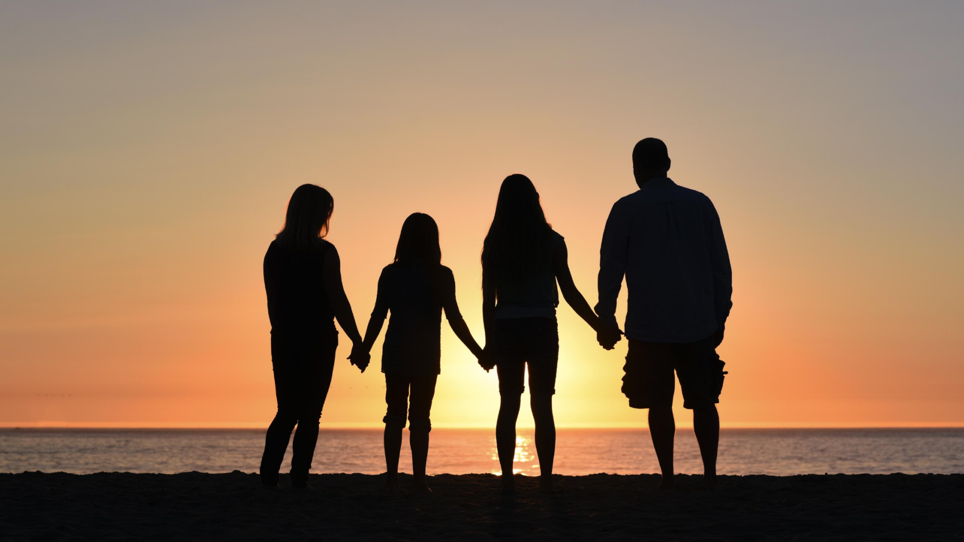 co parenting and unemployment mother, two daughter, and dad holding hands and silhouetted before a sunset