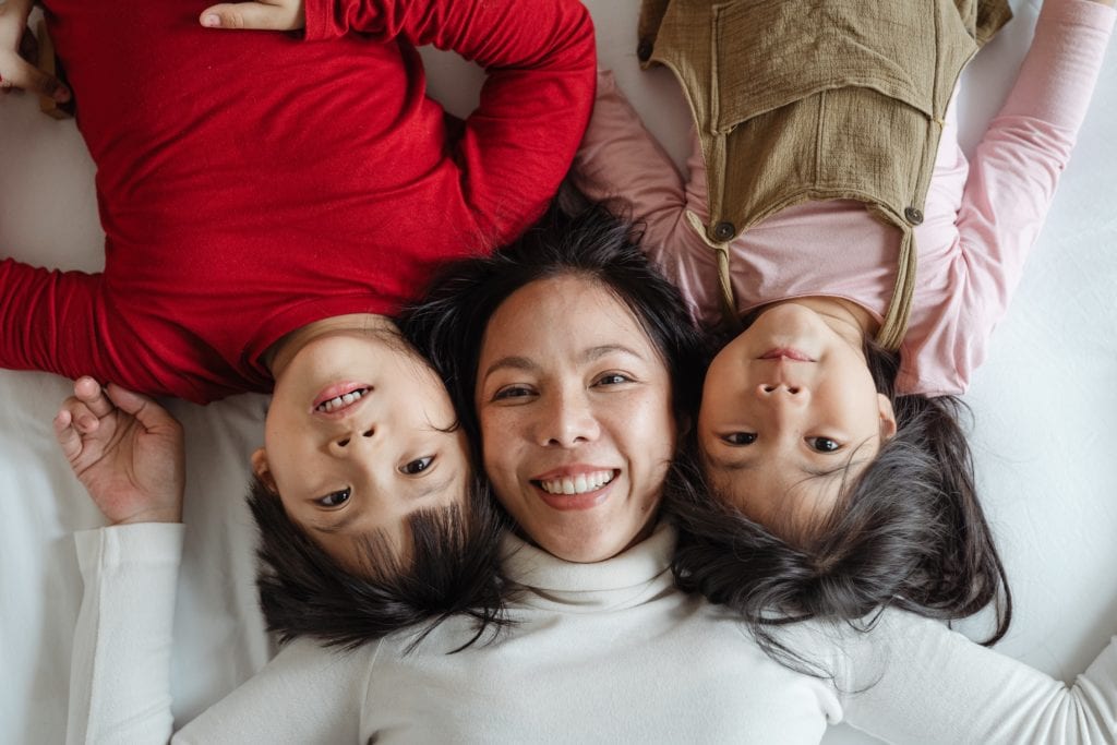 Looking up at the camera, an Asian mother lays between her son and daughter.
